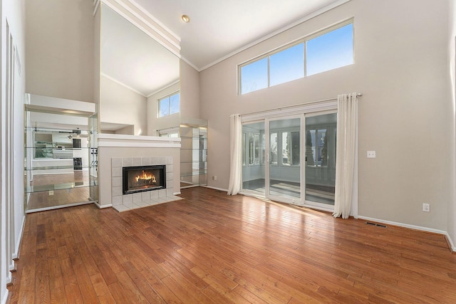 unfurnished living room featuring a tiled fireplace, ornamental molding, hardwood / wood-style floors, and high vaulted ceiling