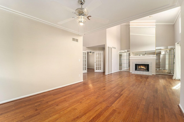 unfurnished living room with french doors, ornamental molding, a tile fireplace, hardwood / wood-style flooring, and ceiling fan