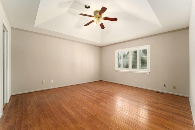 empty room with a raised ceiling, vaulted ceiling, hardwood / wood-style flooring, and ceiling fan