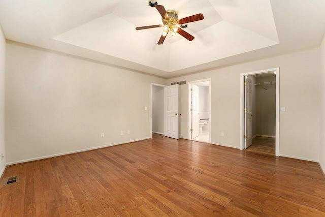 unfurnished bedroom with hardwood / wood-style flooring, a walk in closet, a raised ceiling, and ensuite bathroom