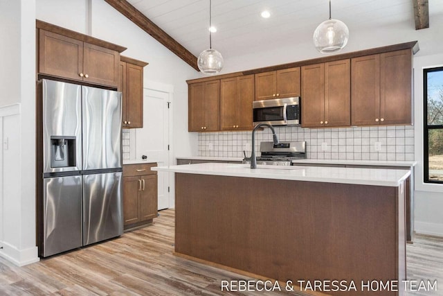 kitchen featuring decorative light fixtures, lofted ceiling with beams, a center island with sink, appliances with stainless steel finishes, and decorative backsplash