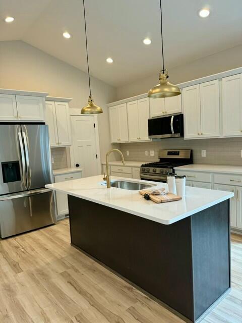 kitchen with decorative light fixtures, an island with sink, white cabinetry, light hardwood / wood-style floors, and stainless steel appliances