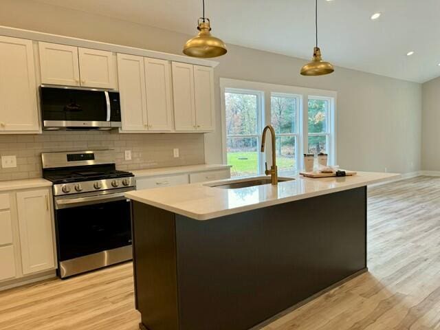 kitchen with a kitchen island with sink, sink, white cabinets, and appliances with stainless steel finishes