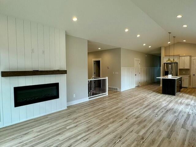 unfurnished living room featuring lofted ceiling, a large fireplace, and light hardwood / wood-style flooring