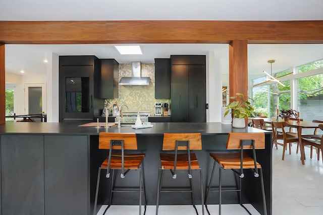 kitchen featuring a peninsula, a skylight, wall chimney range hood, decorative backsplash, and modern cabinets