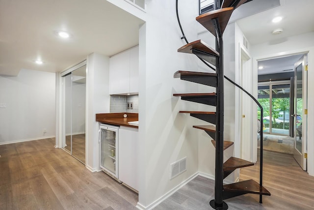 staircase featuring wine cooler, visible vents, and wood finished floors