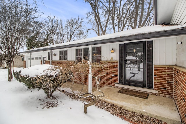 snow covered property entrance with an attached garage and brick siding