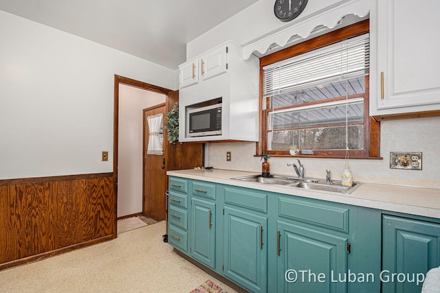 kitchen featuring built in microwave, sink, wooden walls, and white cabinets