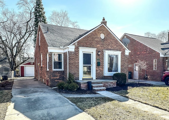 bungalow featuring brick siding, a shingled roof, a detached garage, a chimney, and an outbuilding