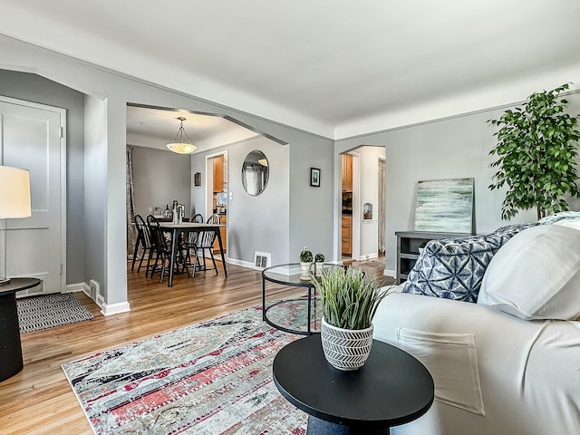 living room featuring arched walkways, visible vents, light wood-style flooring, and baseboards