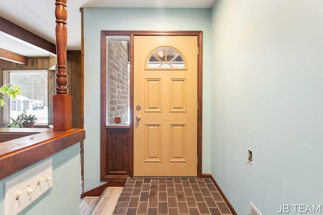 foyer entrance featuring brick floor, baseboards, and beam ceiling