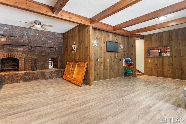 living area featuring wooden walls, light wood-style flooring, ceiling fan, beamed ceiling, and a brick fireplace