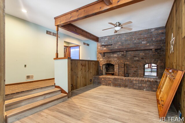 living room featuring beam ceiling, visible vents, a fireplace, and light wood finished floors