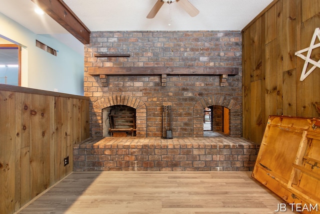 living room with ceiling fan, beamed ceiling, a brick fireplace, and light wood-style floors