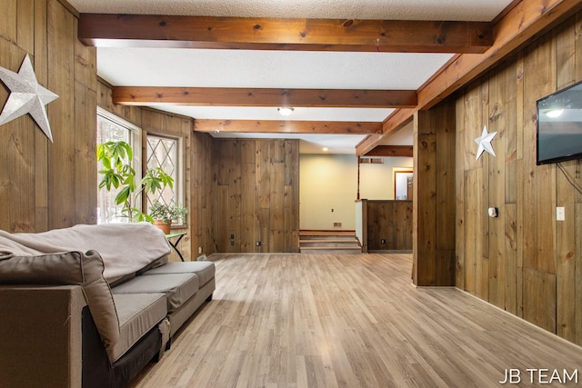 living area with light wood-style floors, wooden walls, beamed ceiling, and a textured ceiling