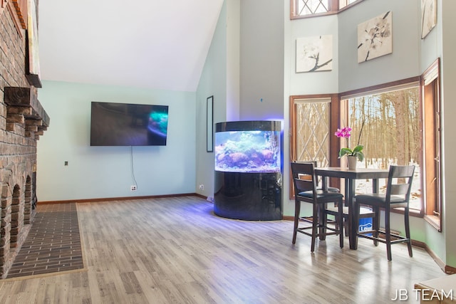 dining space with a fireplace, high vaulted ceiling, and wood finished floors