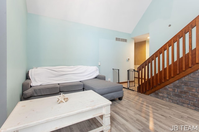 living room with light wood-style floors, stairway, visible vents, and high vaulted ceiling