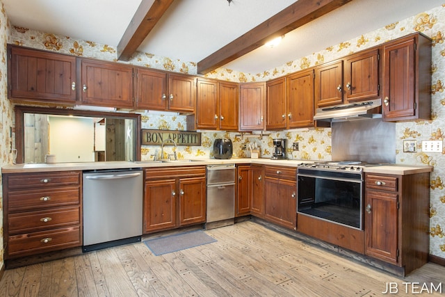 kitchen featuring light countertops, appliances with stainless steel finishes, a sink, under cabinet range hood, and wallpapered walls