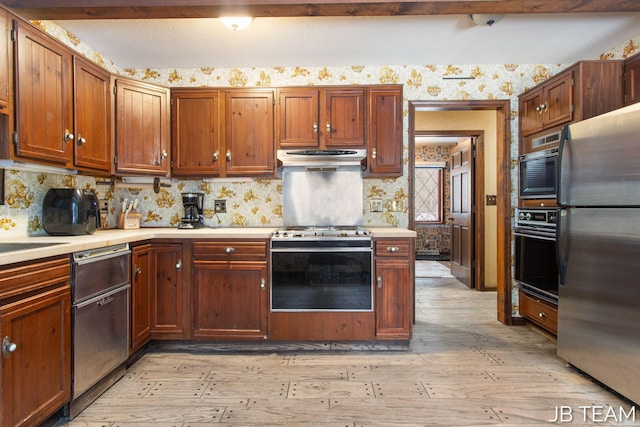 kitchen featuring under cabinet range hood, light wood-style floors, light countertops, appliances with stainless steel finishes, and wallpapered walls