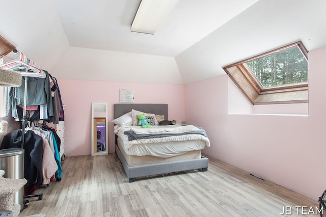 bedroom featuring lofted ceiling with skylight, multiple windows, and light wood finished floors