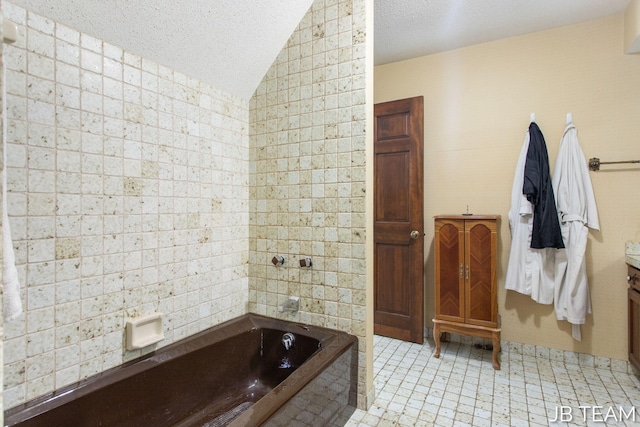 full bathroom featuring a washtub, vaulted ceiling, vanity, and a textured ceiling