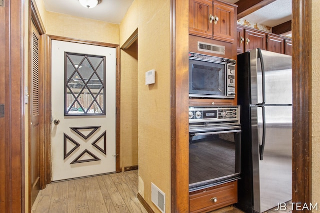 kitchen featuring light wood finished floors, visible vents, appliances with stainless steel finishes, and brown cabinetry