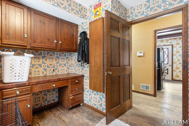 kitchen featuring light wood-style flooring, dark countertops, visible vents, and wallpapered walls