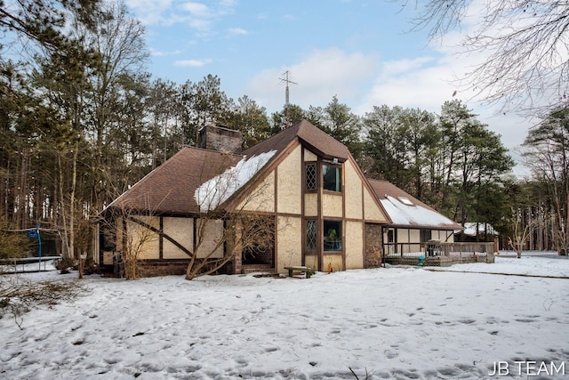 snow covered back of property featuring a chimney and stucco siding