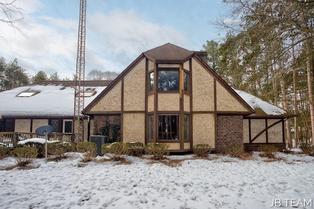 snow covered rear of property featuring a shingled roof and stucco siding