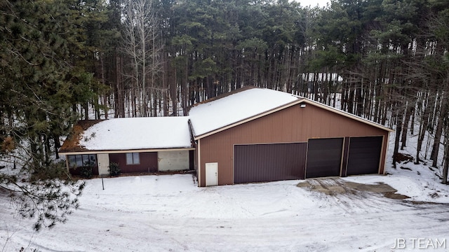 snow covered garage with a detached garage and a view of trees