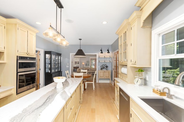 kitchen featuring appliances with stainless steel finishes, pendant lighting, sink, backsplash, and light hardwood / wood-style flooring