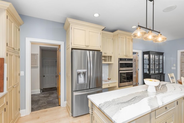 kitchen featuring pendant lighting, stainless steel appliances, cream cabinets, light stone countertops, and a kitchen island