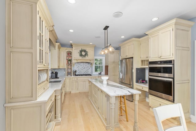 kitchen with pendant lighting, a kitchen breakfast bar, stainless steel appliances, a center island, and cream cabinets