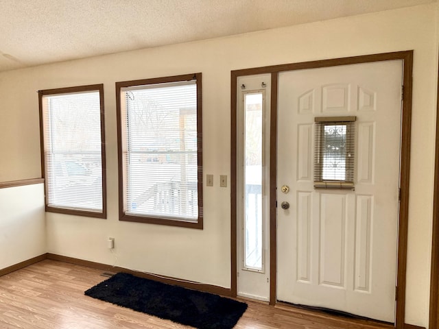 entryway with light wood-type flooring, a textured ceiling, and baseboards