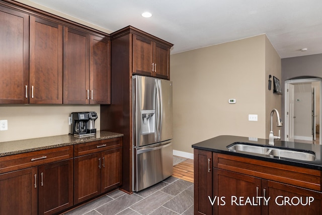 9340 Freedom Dr, West Olive, MI 49460 - kitchen with dark stone countertops, baseboards, arched walkways, stainless steel refrigerator with ice dispenser, and a sink