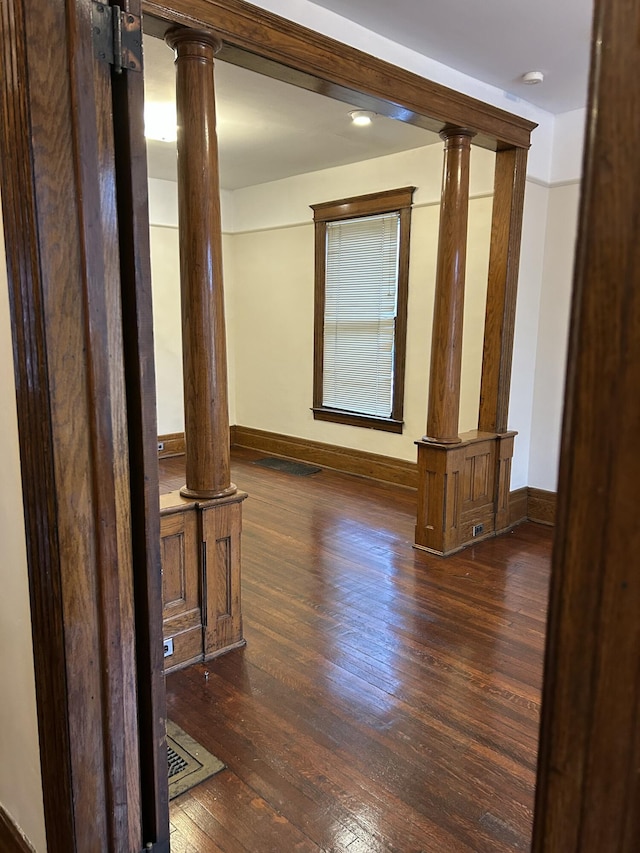 unfurnished room featuring ornate columns and dark hardwood / wood-style flooring