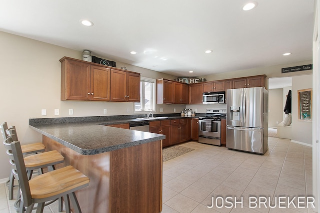 kitchen with sink, a breakfast bar area, light tile patterned floors, kitchen peninsula, and stainless steel appliances