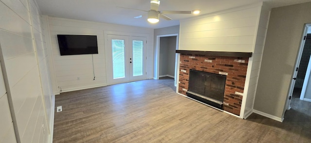 unfurnished living room featuring ceiling fan, a brick fireplace, wood finished floors, and baseboards