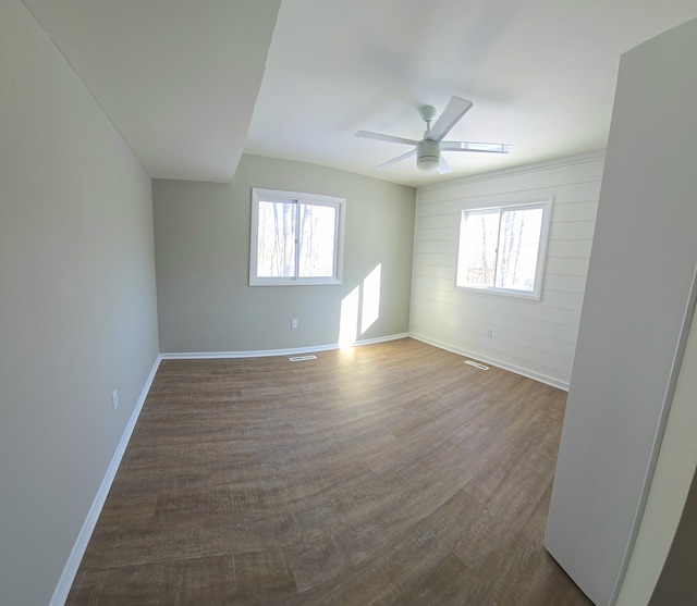 spare room with wooden walls, visible vents, baseboards, dark wood-style floors, and ceiling fan