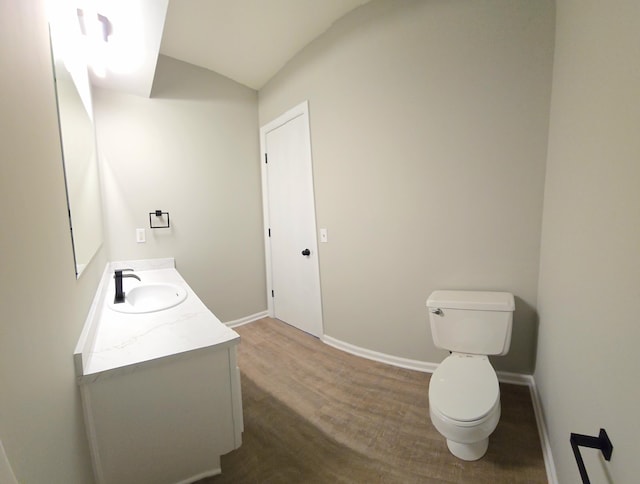 bathroom featuring baseboards, lofted ceiling, toilet, wood finished floors, and vanity