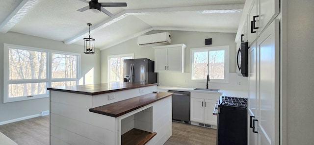 kitchen featuring wooden counters, a wall mounted AC, appliances with stainless steel finishes, a kitchen island, and a sink