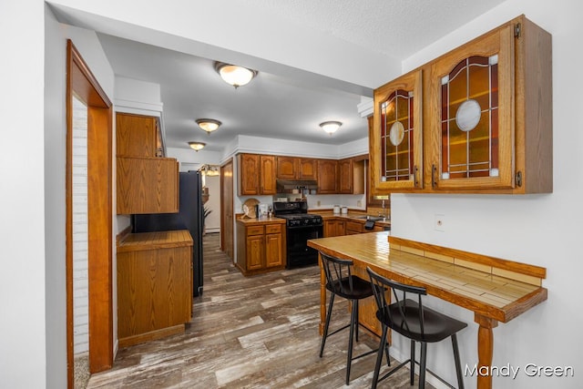 366 E Beech St NE, Cedar Springs, MI 49319 - kitchen featuring black appliances, brown cabinets, dark wood-style flooring, glass insert cabinets, and under cabinet range hood