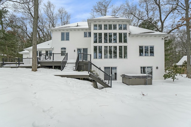 snow covered house featuring a wooden deck and a hot tub