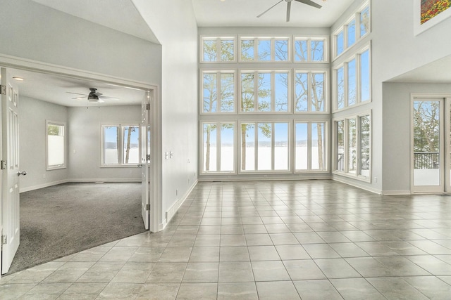 unfurnished living room featuring ceiling fan, light tile patterned floors, a towering ceiling, and a healthy amount of sunlight