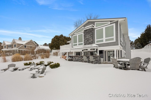 snow covered rear of property featuring stone siding, stairs, and fence