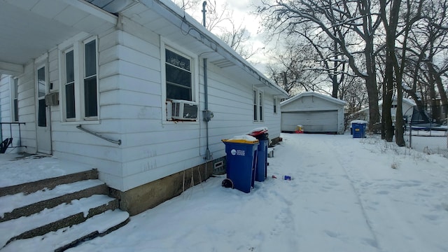 view of snow covered exterior featuring an outbuilding, cooling unit, and a garage