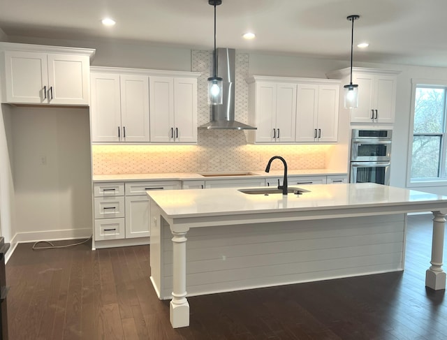 kitchen featuring a center island with sink, sink, hanging light fixtures, and wall chimney range hood