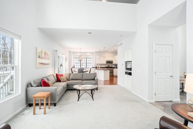 living area featuring light colored carpet, baseboards, visible vents, and a towering ceiling