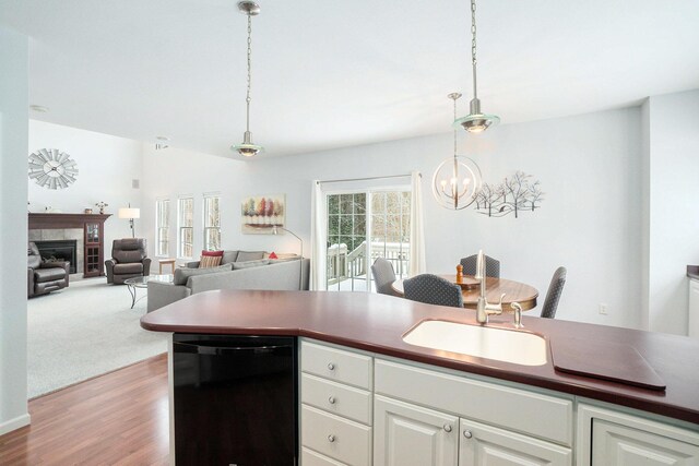kitchen featuring dark countertops, a chandelier, black dishwasher, a fireplace, and a sink