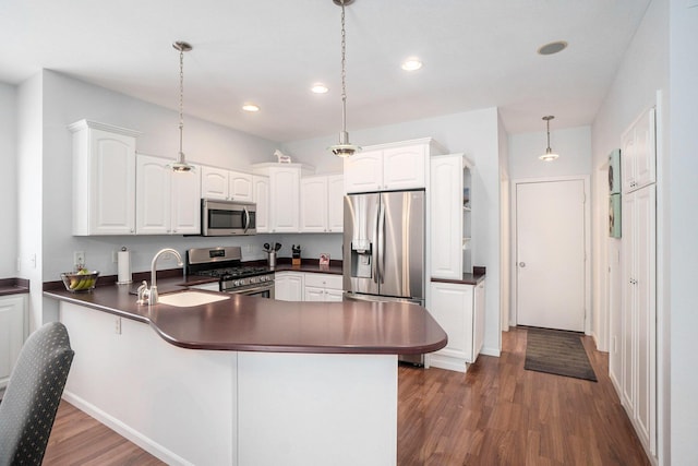 kitchen with dark countertops, a peninsula, stainless steel appliances, and a sink